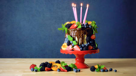 Delicious birthday chocolate drip cake decorated with fresh seasonal fruit and berries with burning candles.の写真素材