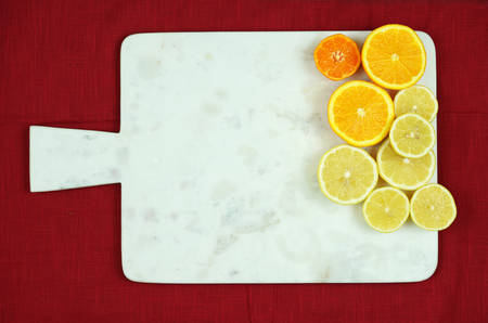 White marble cutting board with citrus fruit halves on red tablecloth and copy space.
