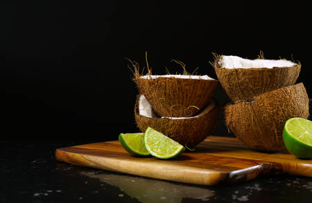 Coconut halves and limes spotlighted against a black background.