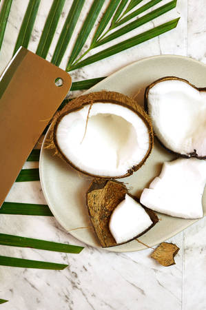 Coconut cut into pieces on plate on marble table top, creative flat lay.