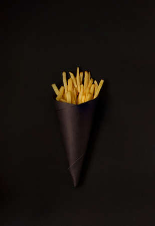 french fries on a black background, in a black package, vertical