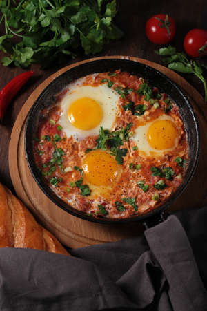 fried eggs with stewed tomatoes , cast iron pan , on a wooden table,top view , rustic, verticalの写真素材