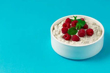 Bowl yogurt with raspberries and mint, on a blue background, no people, copy spase, horizontal,