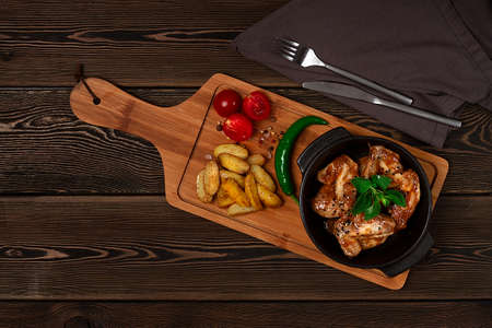 Chicken wings, fried, barbecue, with potatoes, on a chopping board, cherry and pepper, wooden table, top view, no people,の写真素材