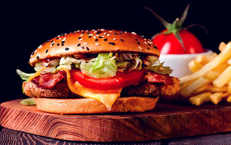 Burger with chicken cutlet fried bacon and vegetables, French fries, glass of beer, on a wooden...
