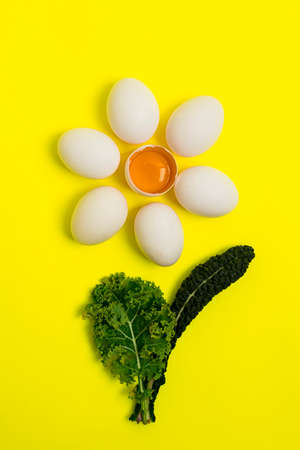 Fresh eggs, on a yellow background, in the shape of a chamomile with cabbage leaves, top view, vertically, without people, food background.の写真素材