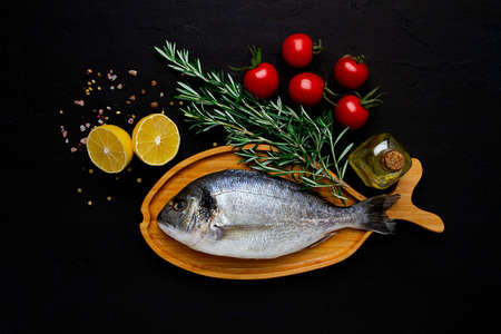 Raw fresh dorado fish, wooden plate in the shape of a fish, on a black table, with ingredients, top view, no people,の写真素材