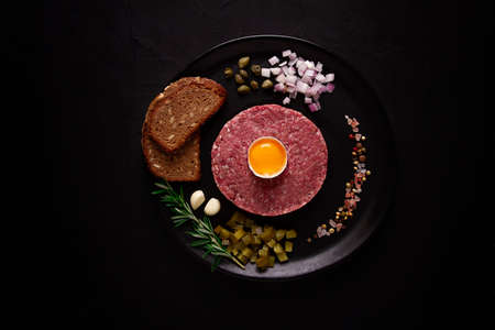 Beef tartare, with egg capers, gherkins and bread, on a black background, top view, close up, horizontal, no people,の写真素材
