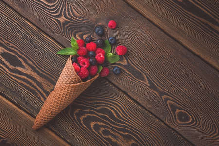 Waffle chocolate cone with fresh berries and mint, on a wooden table, top view, rustic style, toned,の写真素材