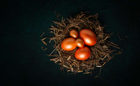 Golden Easter eggs on straw, dark green background, top view, food background,
