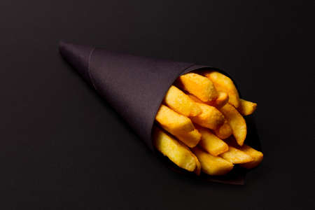 french fries in black paper packaging, on a black background, close-up, selective focus,