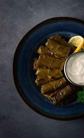 Dolma, cabbage rolls, grape leaves with filling, white sauce, lemon and herbs, rustic, selective...