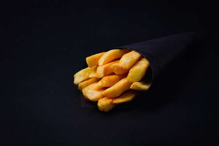 french fries, in black paper packaging,on a black background, close-up, selective focus,