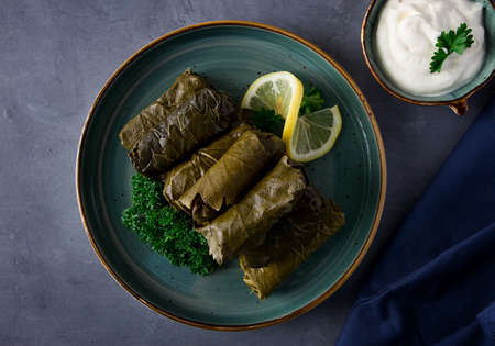 Dolma, cabbage rolls, grape leaves with filling, white sauce, lemon and herbs, rustic, selective...