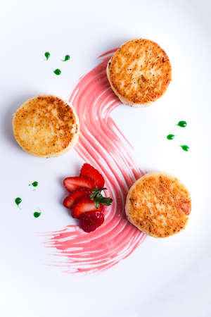 Cottage cheese pancakes, on a white plate decorated with sauce, fresh strawberry berry, close-up, no people,の写真素材