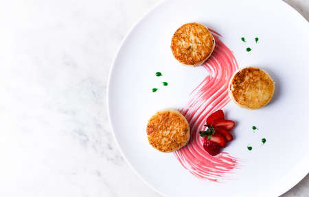 Cottage cheese pancakes, on a white plate decorated with sauce, fresh strawberry berry, close-up, no...