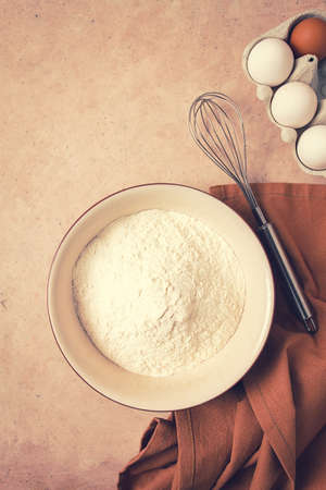 Food background concept, plate with wheat flour, whisk for whipping, kitchen towel, on a beige table, top view, rustic,の写真素材