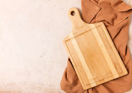 Cutting board beige, unpainted, with a kitchen towel, on a beige background, top view,
