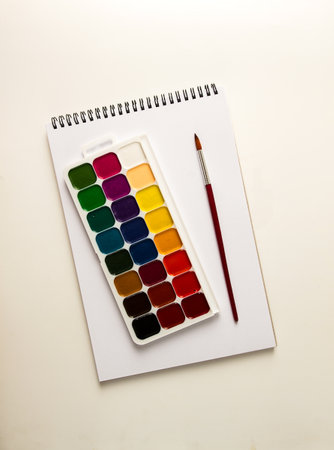 Sketchbook with a palette of watercolor paints, and brushes, top view, no people, on a white background,の写真素材