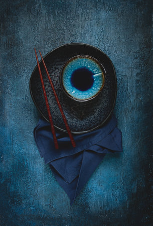 food background, with an empty black plate, a bowl, wooden chopsticks, with a napkin, on a blue background, table setting, top view, no people,の写真素材