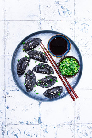 Japanese gyoza dumplings, made of black dough, black gyoza, with green onions and sauce, on a plate, close-up,の写真素材