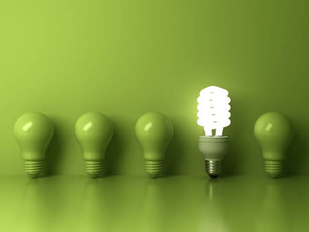 Eco energy saving light bulb , one glowing compact fluorescent lightbulb standing out from unlit incandescent bulbs reflection on green background , individuality and different concept . 3D rendering.の写真素材