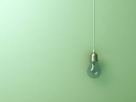 One hanging turn off incandescent light bulb on green wall background with blank space , creative...