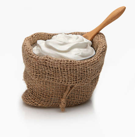 a bowl of greek yogurt in a small rustic sack on a white background.A wooden spoon is in it as well, ready to serve.の写真素材