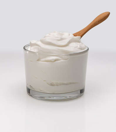 a bowl of greek yogurt on a white background.A wooden spoon is in it as well, ready to serve.の写真素材