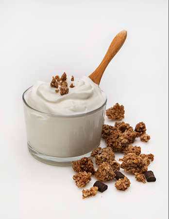 a bowl of greek yogurt with dark chocolate granola on a white background.A rustic spoon is in it as well, ready to serve.の写真素材