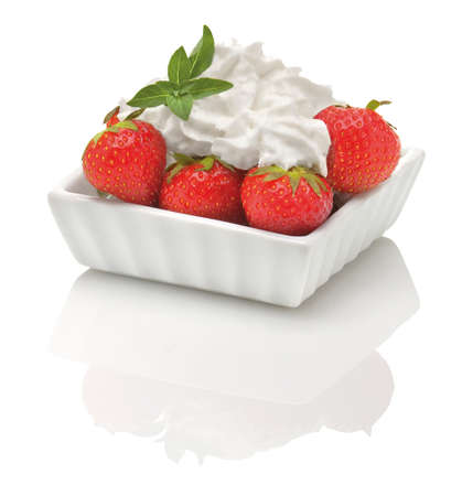 a stack of fresh strawberries with a whipped cream topping and some peppermint leaves in a white bowl, isolated on a white background,studio shot with a reflectionの写真素材
