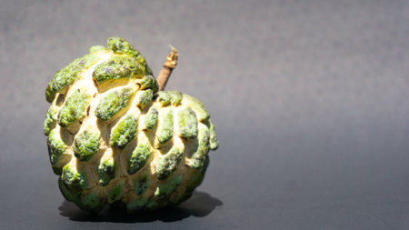 A green custard apple (Annona squamosa Linn) with a black background. It is in the left corner.