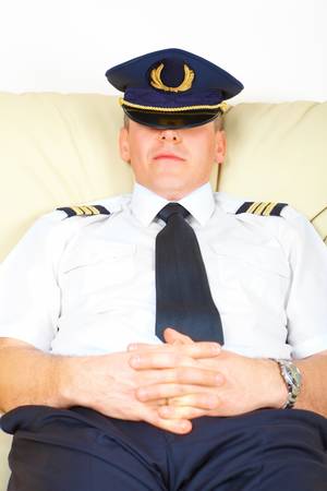 Commercial pilot wearing uniform with epaulettes and hat half sitting idly, resting or stiking.の写真素材