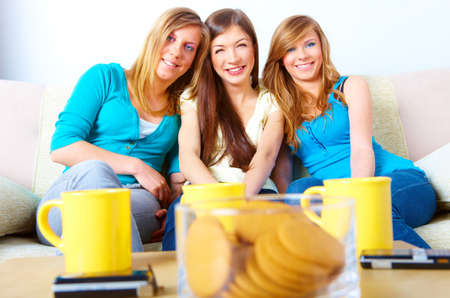 Three happy friends beautiful girls sitting on sofa in home with cups, cookies and phones in the foreground. の写真素材