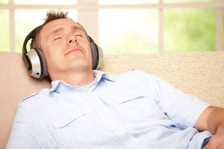 Man listening music with cordless headphones sitting on sofa at home
の写真素材