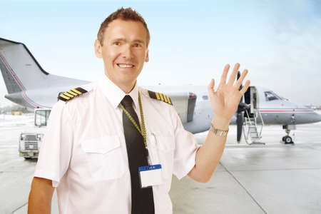 Airline pilot wearing uniform with epaulettes waving, with passenger aircraft in background