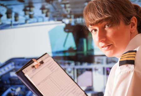 Beautiful woman pilot wearing uniform with epauletes and headset with notepad inside airliner