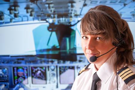 Beautiful woman pilot wearing uniform with epauletes, headset sitting inside airliner with visible cockpit during flight の写真素材
