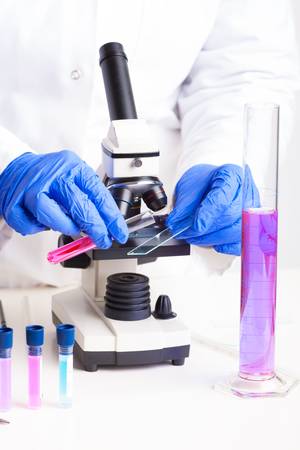 Lab technician working with equipment  tweezers, microscope, test tubes  filled with colored fluid, chemical flasksの写真素材