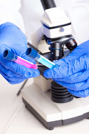 Lab technician working with equipment  tweezers, microscope, test tubes  filled with colored fluid, chemical flasksの写真素材