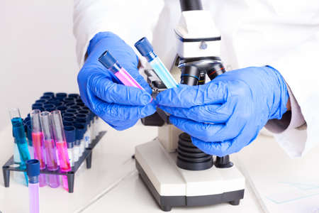 Lab technician working with equipment  tweezers, microscope, test tubes  filled with colored fluid,...