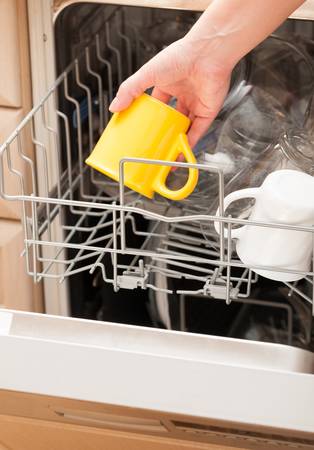 Hand putting a yellow mug into a dishwasher
