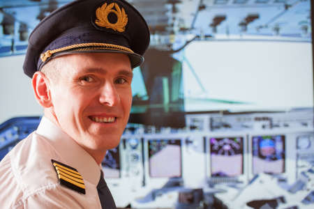 Pilot captain  wearing uniform with epauletes, hat with golden wings sitting inside airliner with visible cockpit during flight の写真素材