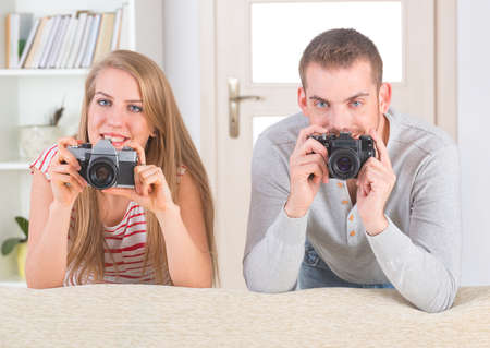 Young couple at home taking pictures with old analog SLR camerasの写真素材