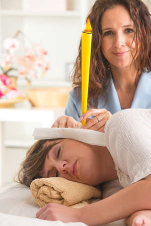 terapist doing ear candling on beautiful woman