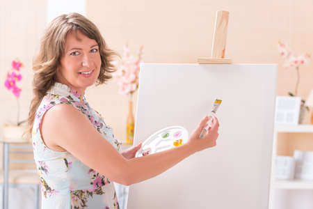 Beautiful woman painting on canvas at her home or workshopの写真素材