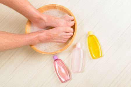 Male feet in a bowl with water and soap, cosmetics in bottles, hygiene and spa conceptの写真素材