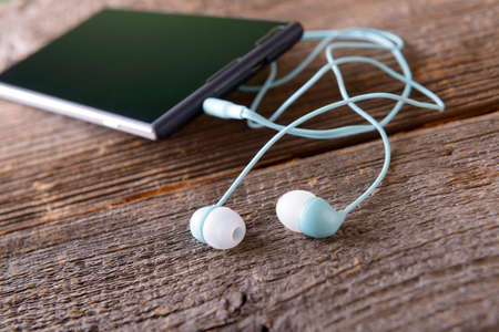 Small headphones with mobile phone on wooden desk
