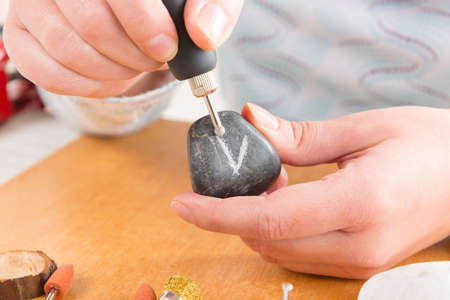 Woman using a high speed rotary multi tool to engrave ornament on the stone
