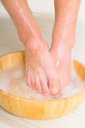 Male feet in a bowl with water and soap, hygiene and spa conceptの写真素材